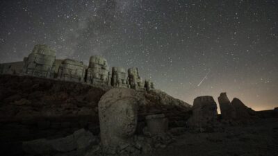 Ilustrasi lintasan meteor di langit malam yang gelap dengan latar belakang rasi bintang.